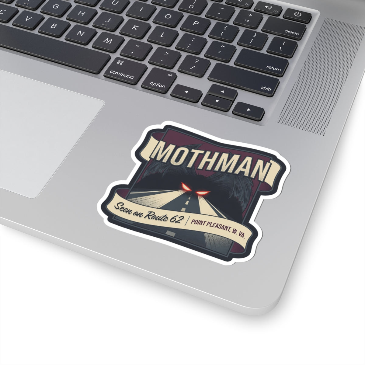 Mothman die-cut sticker on a laptop keyboard: road scene, red eyes, Route 62, Point Pleasant W.Va.