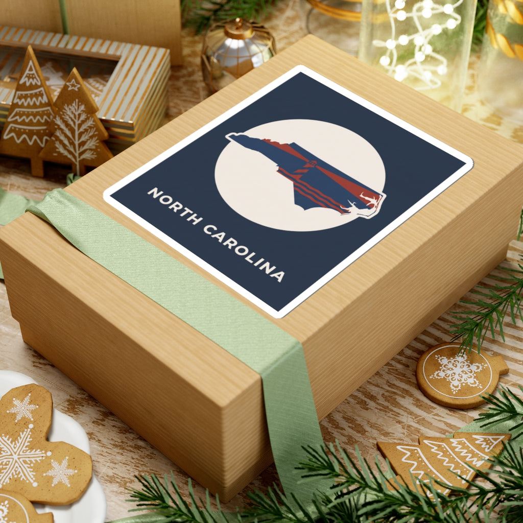North Carolina state kiss-cut sticker on wrapped gift, navy square with map and text