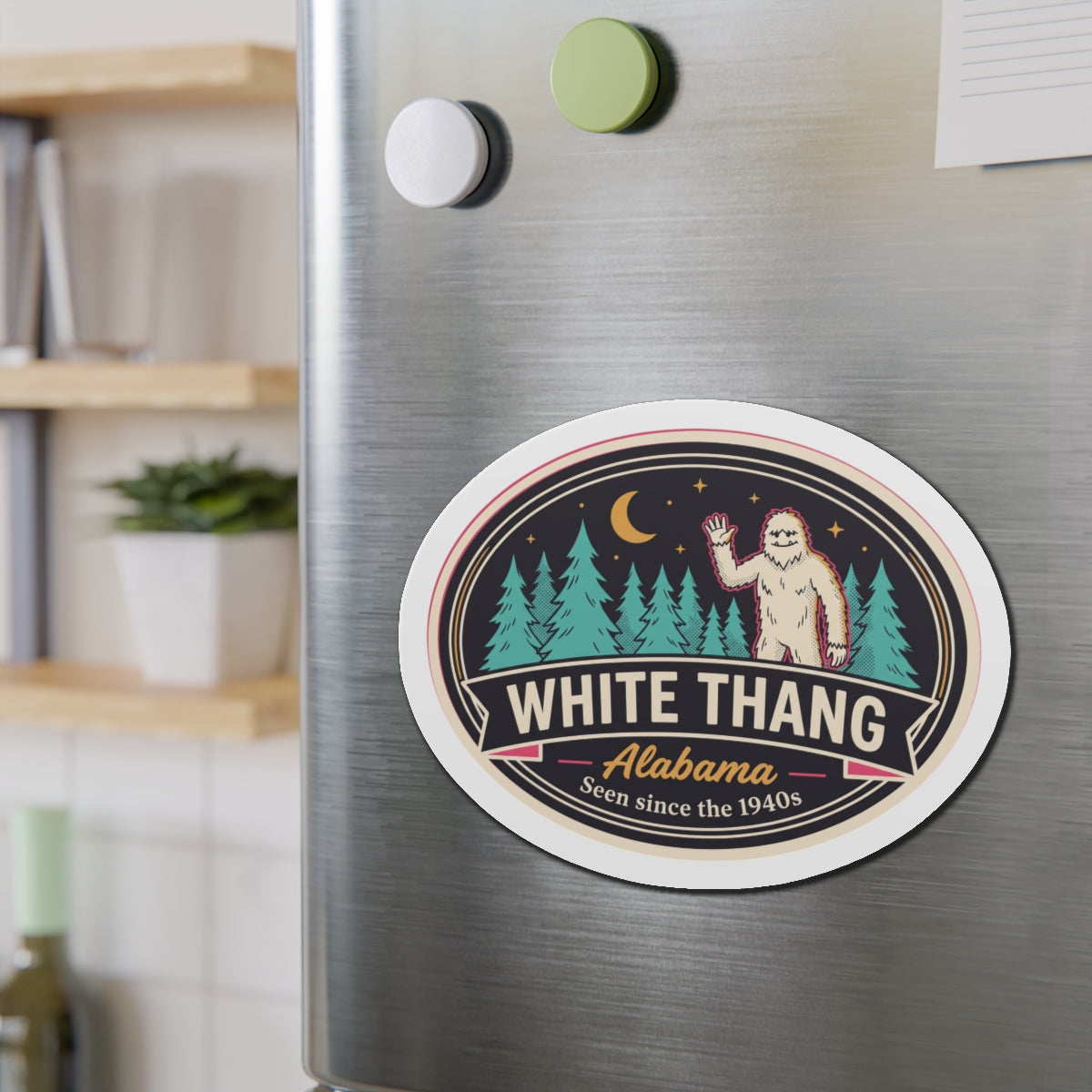 Round die-cut magnet featuring White Thang Alabama badge with Bigfoot standing in evergreen forest