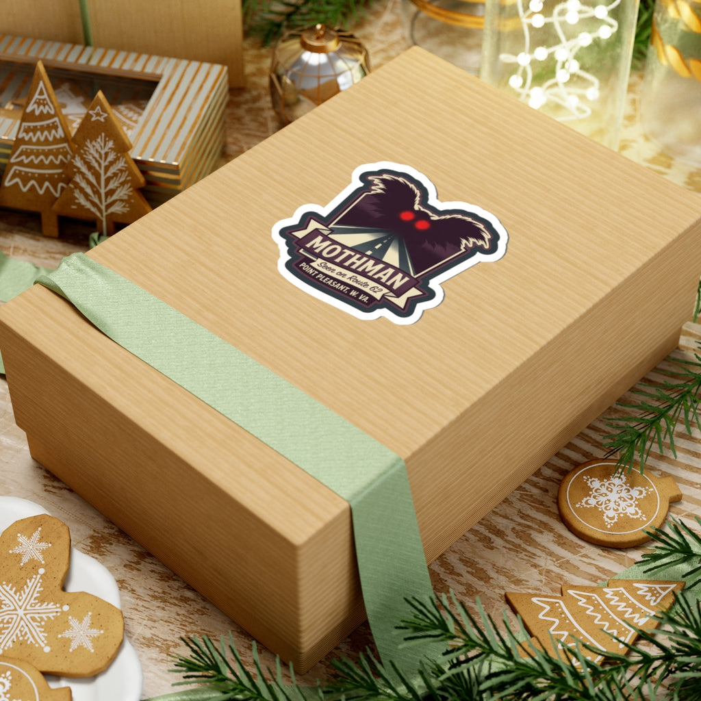 Kiss-cut Mothman sticker on a wrapped gift box, showing red eyes and Route 62 text