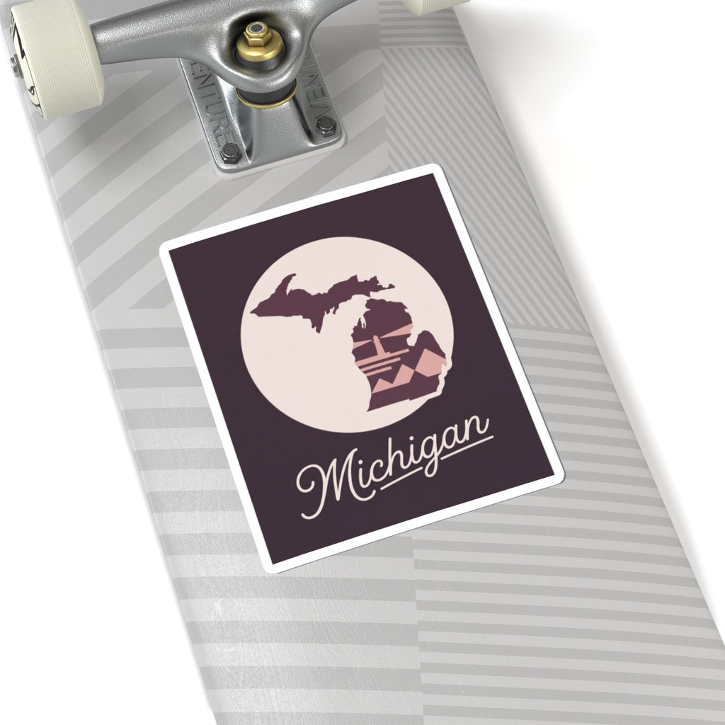 Square Michigan kiss-cut decal on a suitcase: purple state map and lighthouse with cursive “Michigan”.