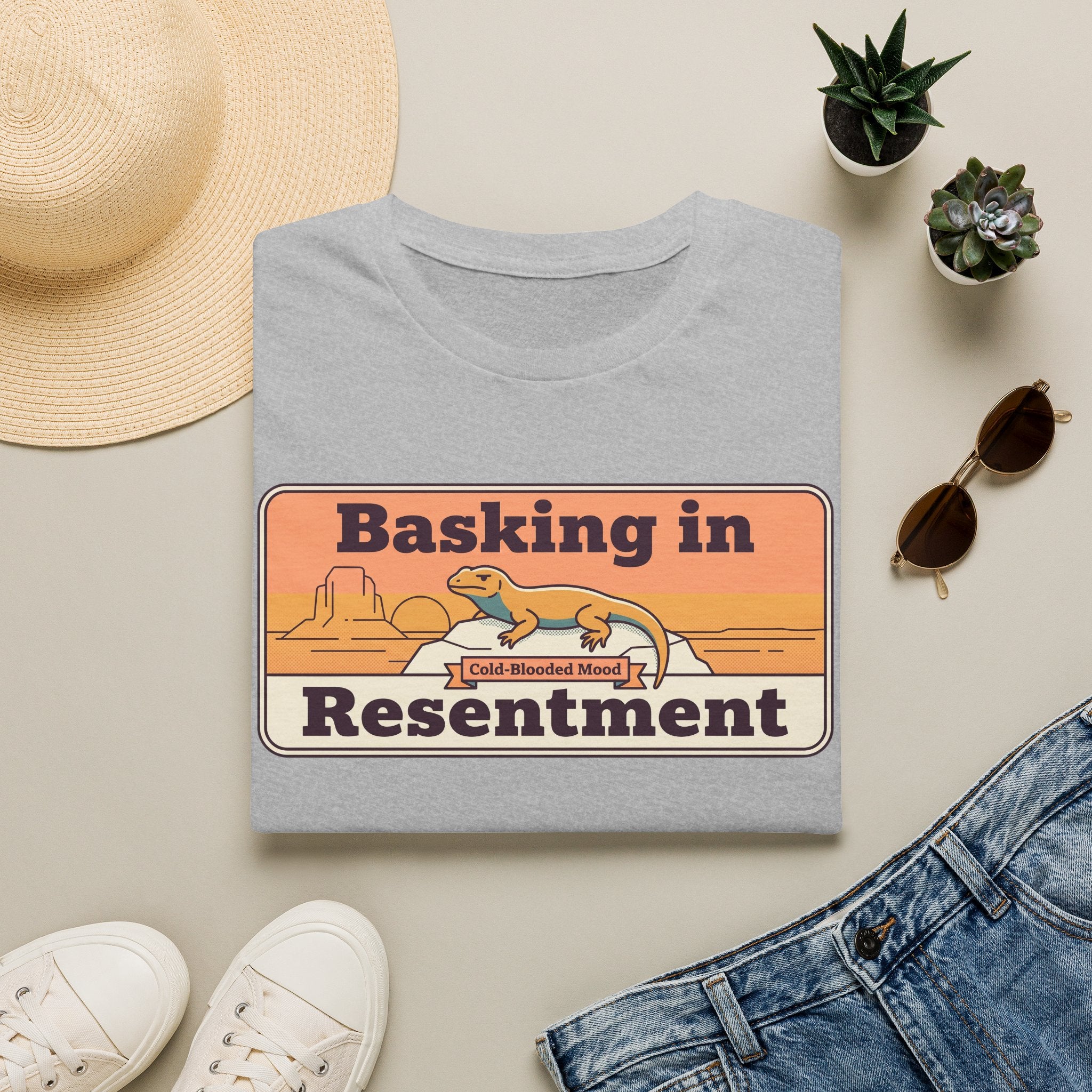 Light gray lizard graphic T-shirt with retro desert print: “Basking in Resentment”.