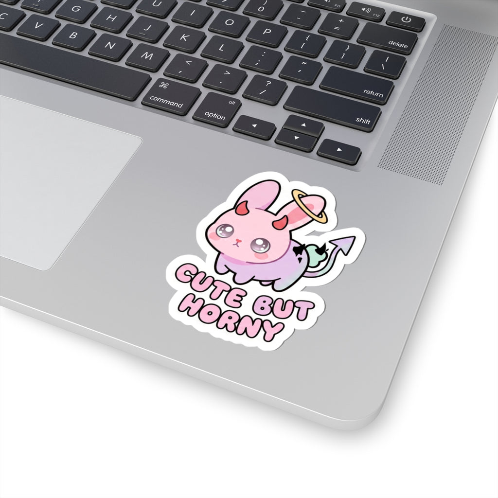 Demon bunny kiss-cut sticker on laptop lid, pastel pink face with 'Cute But Horny' text