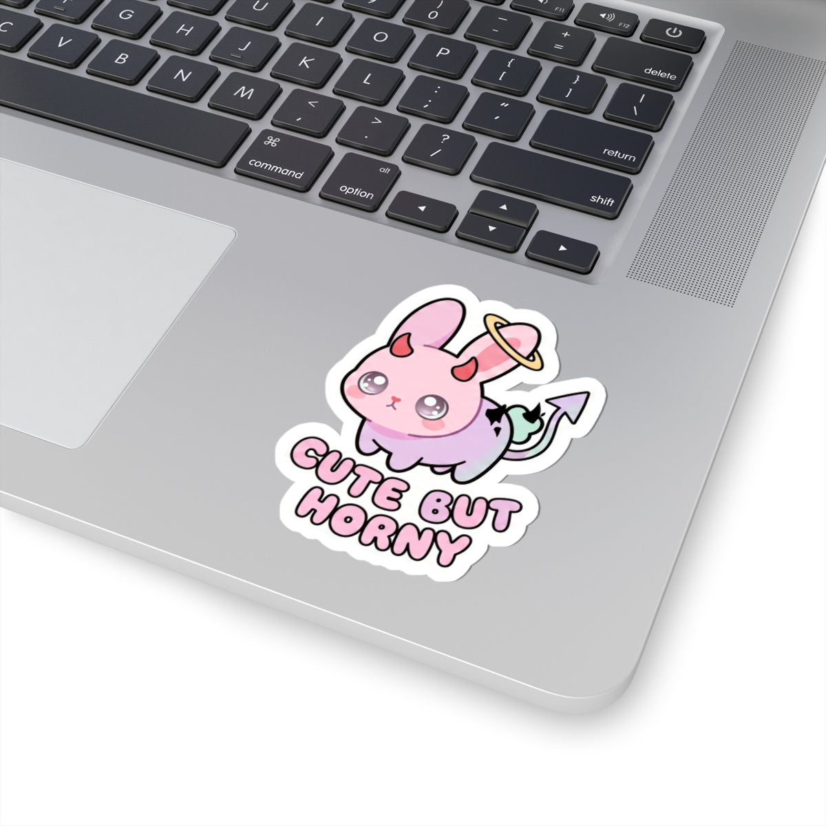 Demon bunny kiss-cut sticker on laptop lid, pastel pink face with 'Cute But Horny' text