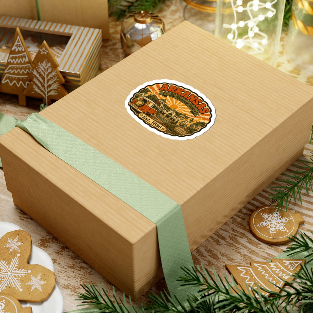 Round Arkansas travel sticker on a wrapped gift box, with orange camper van and “Est. 1836”