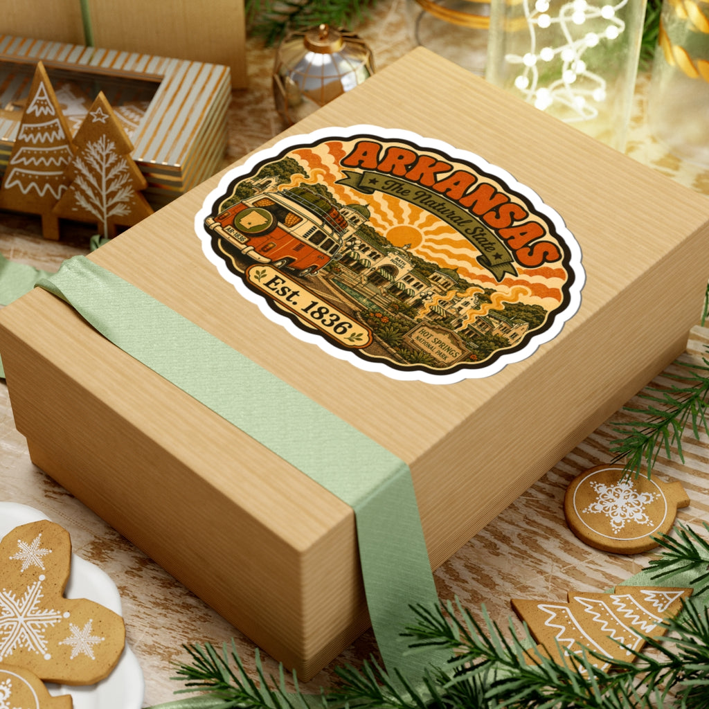 Round Arkansas travel sticker on a gift box, with orange camper van and “Est. 1836”