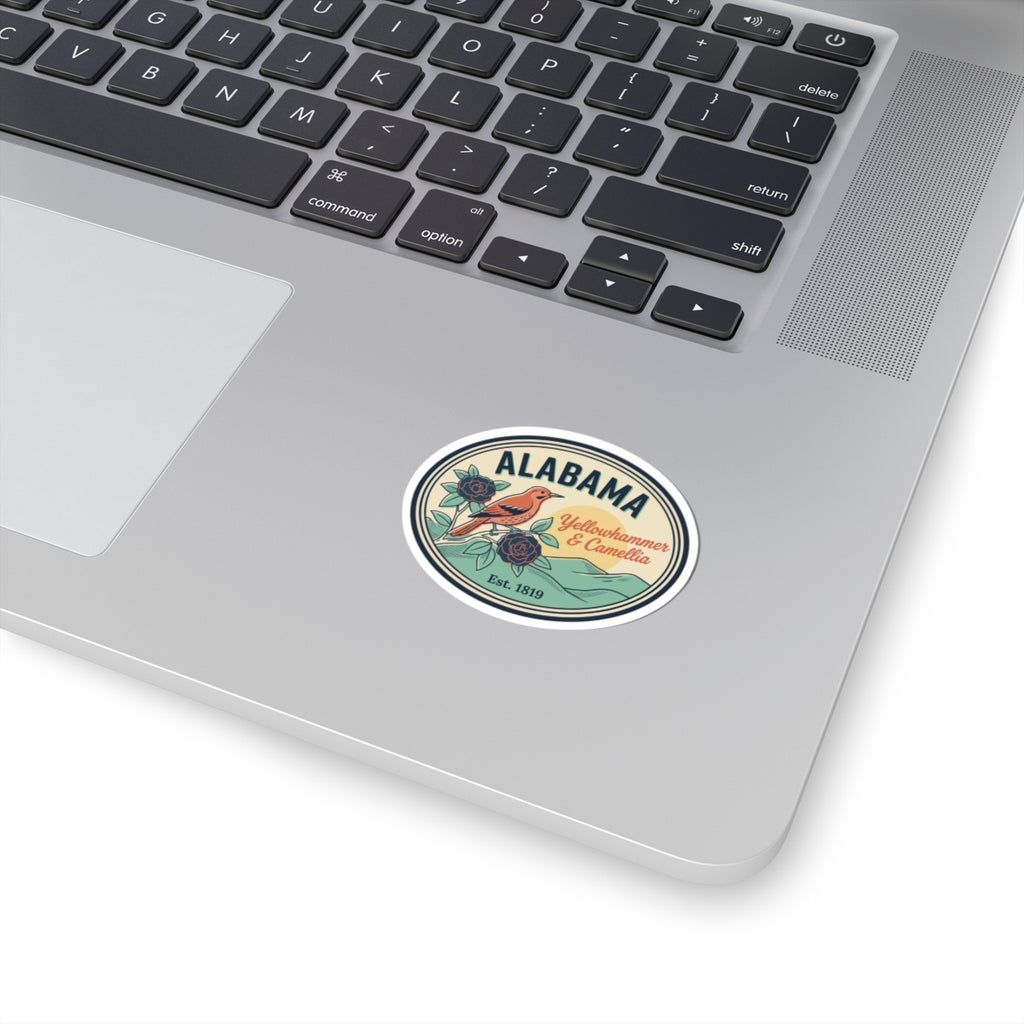 Alabama oval badge sticker on laptop lid, green and teal floral graphic with text.