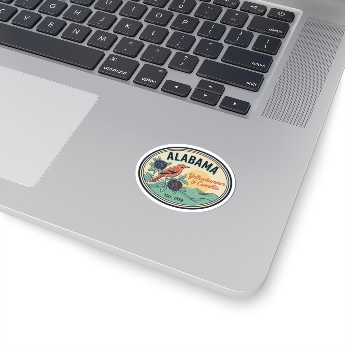 Alabama oval badge sticker on laptop lid, green and teal floral graphic with text.