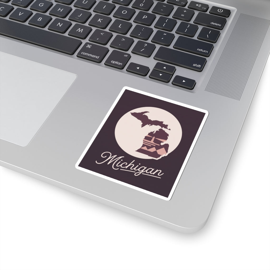 Square Michigan kiss-cut decal on a laptop keyboard: purple map, lighthouse, and “Michigan” script.