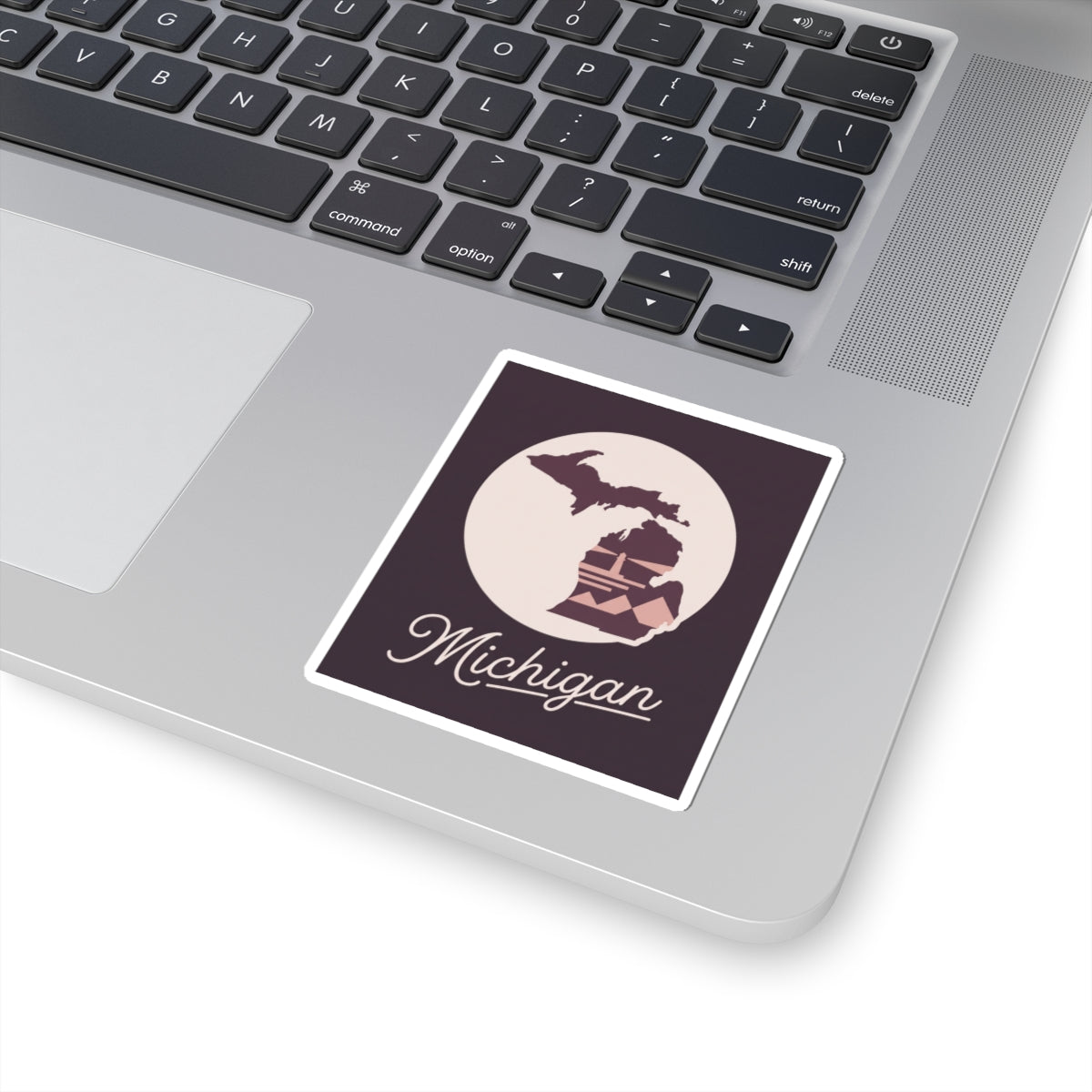 Square Michigan kiss-cut decal on a laptop keyboard: purple map, lighthouse, and “Michigan” script.