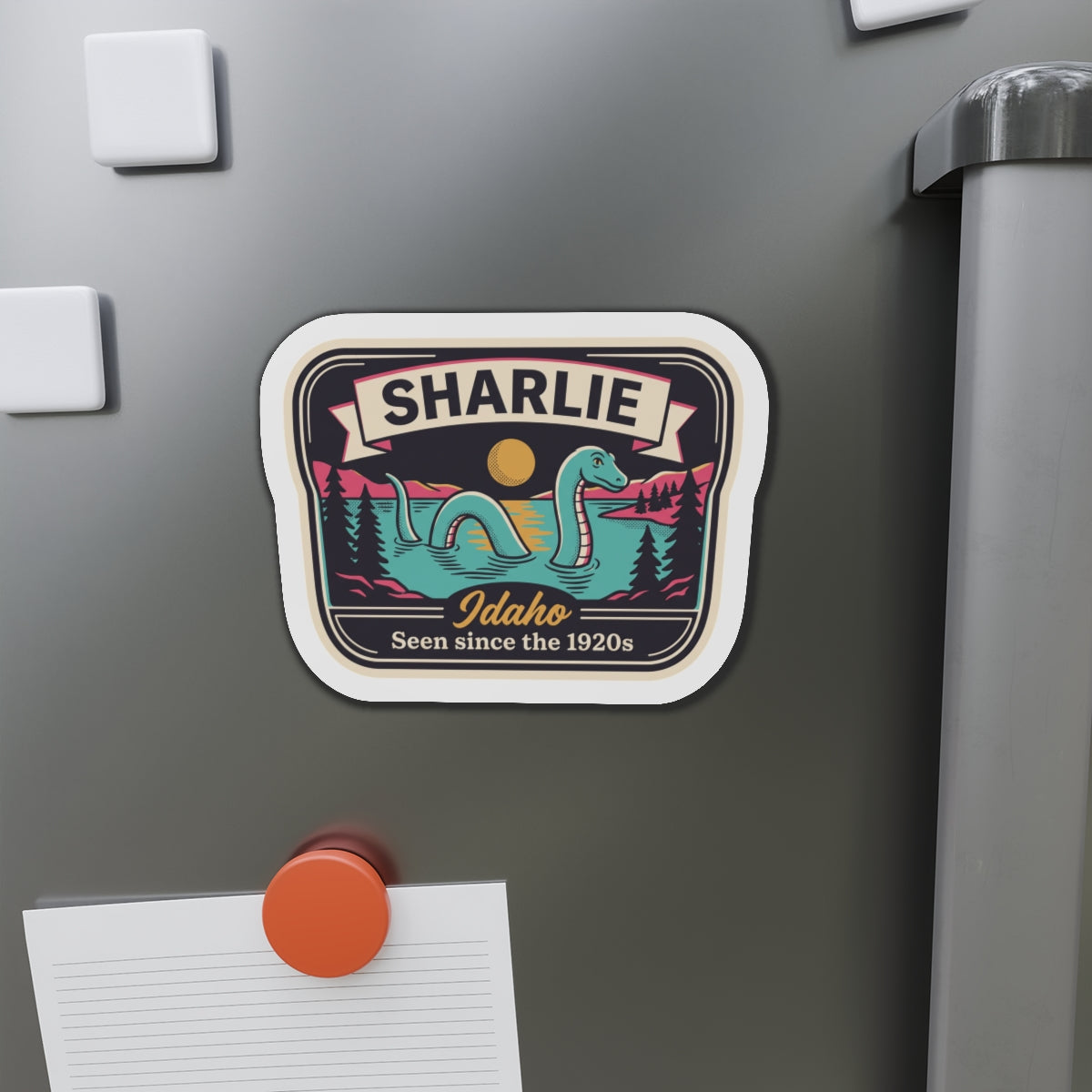 Rounded die-cut magnet showing SHARLIE Idaho badge with teal sea-serpent illustration