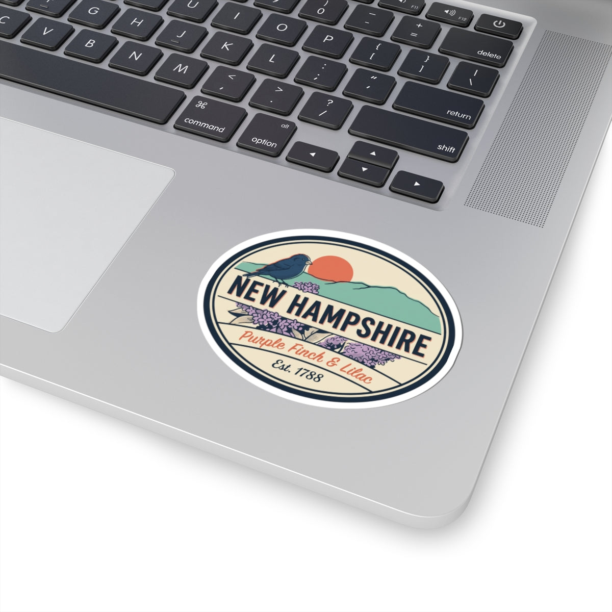 Round New Hampshire sticker on a laptop: purple finch, lilac flowers, Est. 1788
