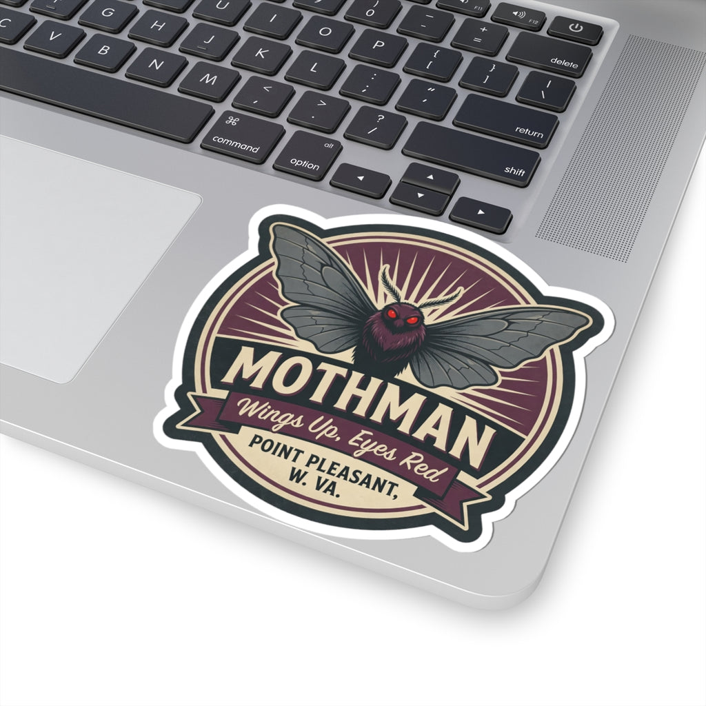 Mothman emblem kiss-cut sticker on laptop surface, close view of wings and red eyes badge