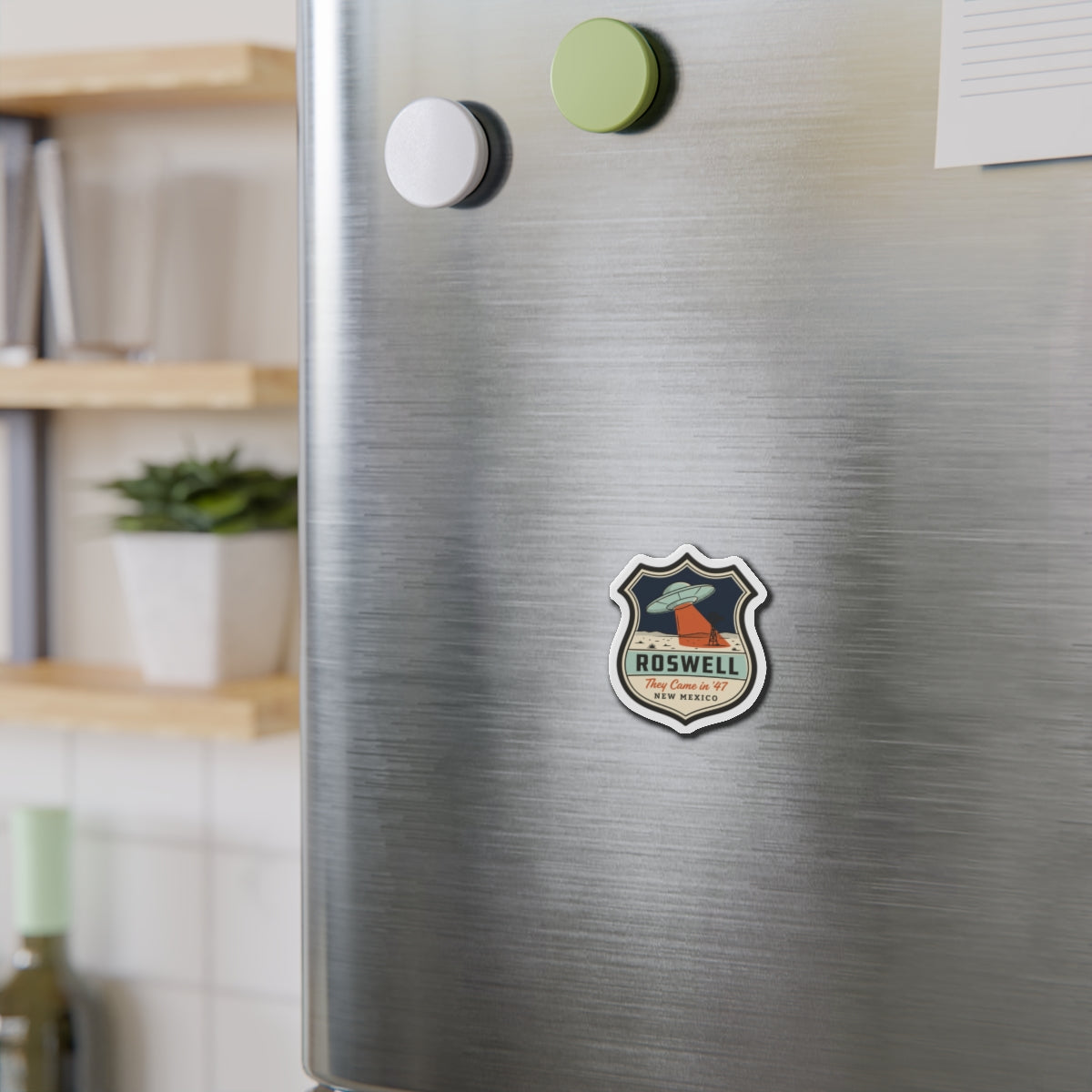 Roswell UFO badge die-cut magnet centered on brushed stainless fridge surface
