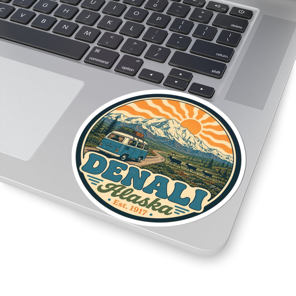 Round Denali Alaska sticker on a laptop, showing mountain peaks, sun rays, and teal van