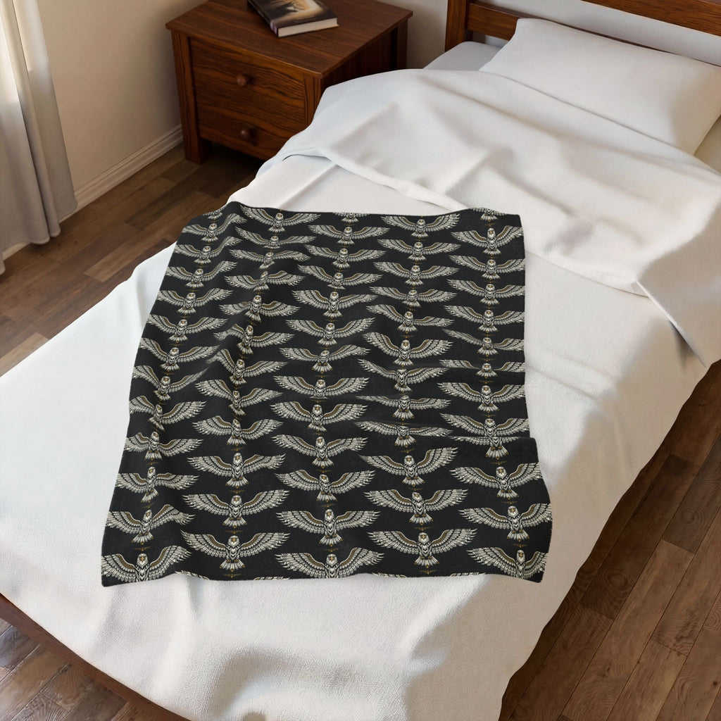 Velveteen plush blanket, black with repeating winged skull pattern in gold, folded on bed