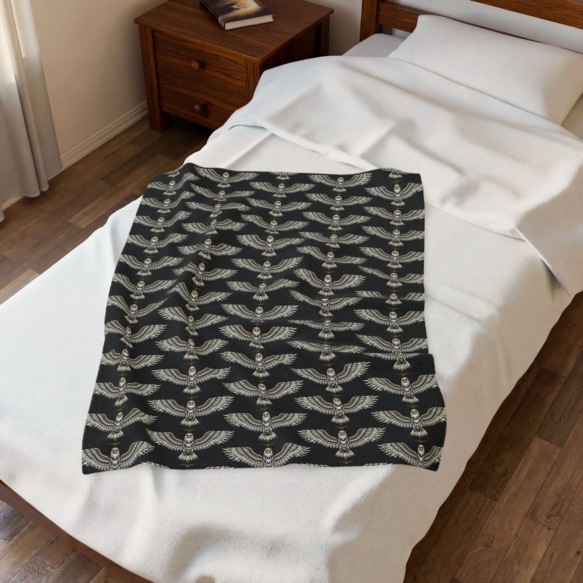 Velveteen plush blanket, black with repeating winged skull pattern in gold, folded on bed