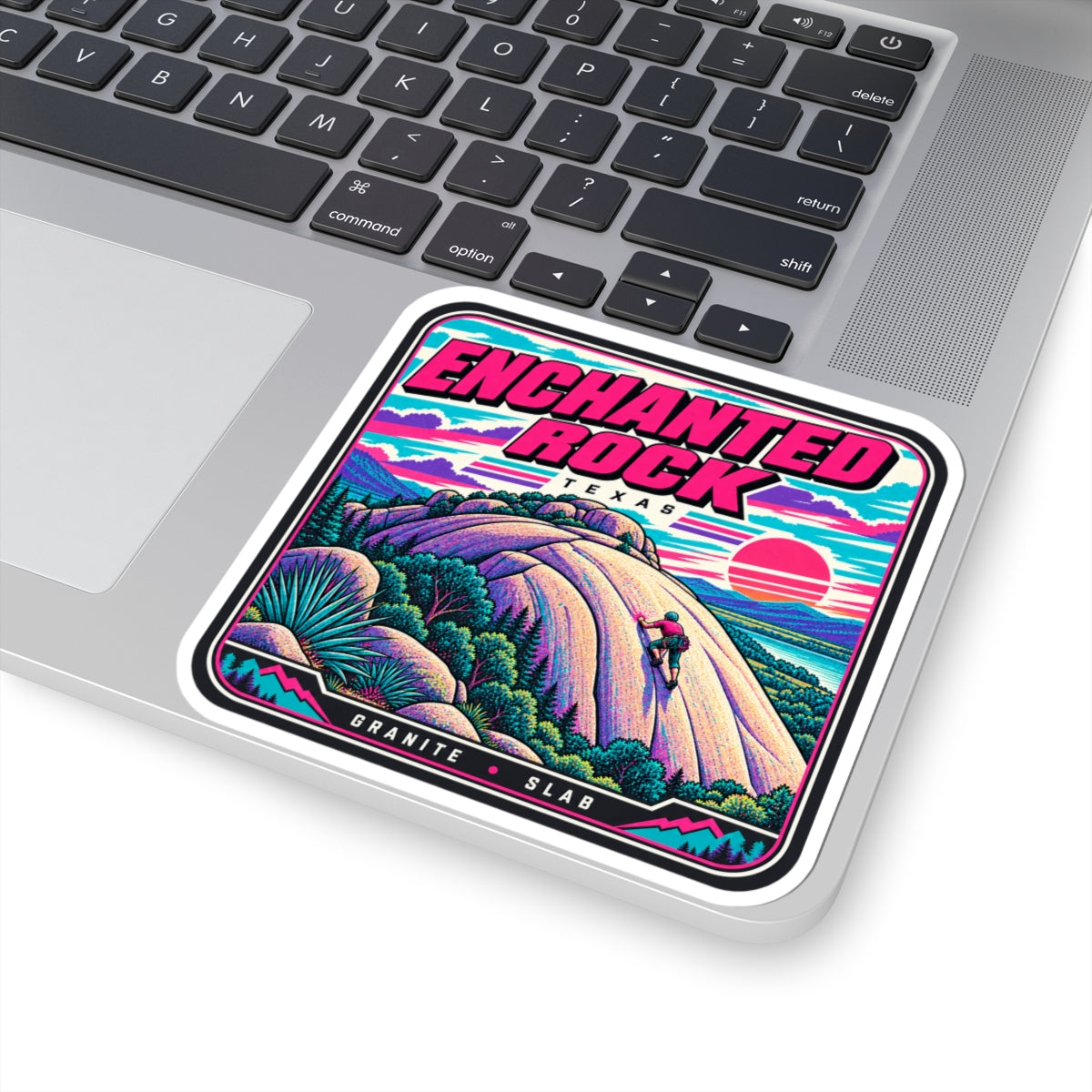 Square kiss-cut sticker on laptop trackpad area, “ENCHANTED ROCK” landscape artwork