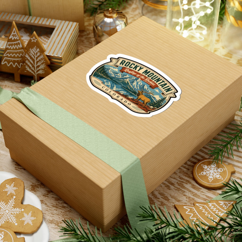 Travel sticker on a wooden gift box, featuring Rocky Mountain title, elk, and Colorado