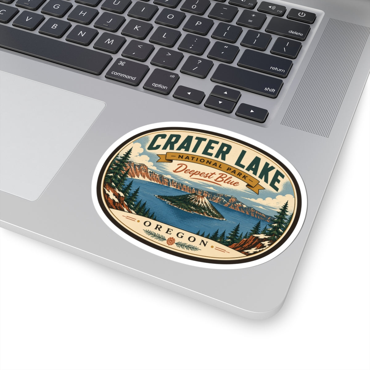 Round travel sticker on laptop keyboard area showing Crater Lake island and “Oregon.”
