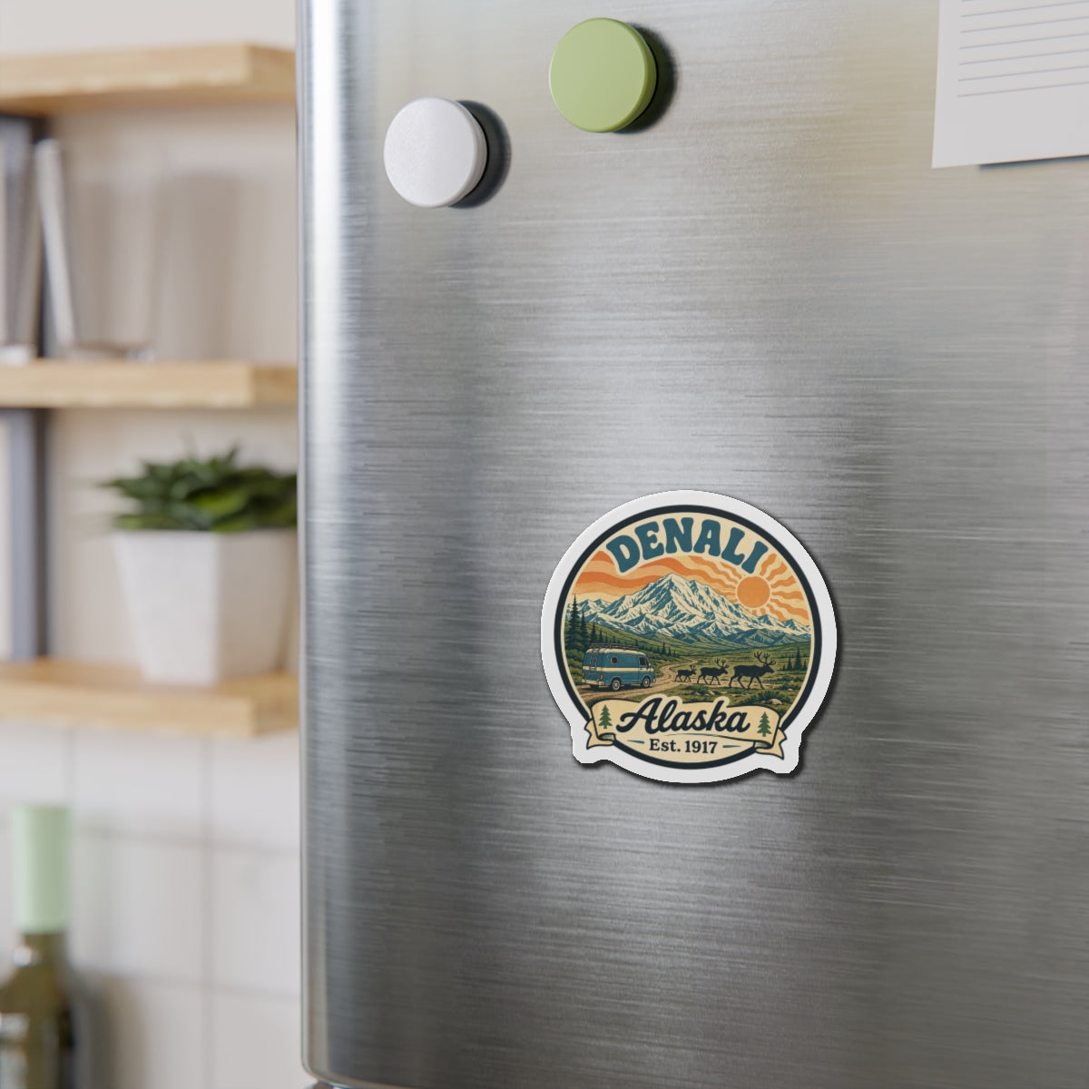 Denali Alaska die-cut magnet on stainless fridge door, small round design with "Alaska Est. 1917"