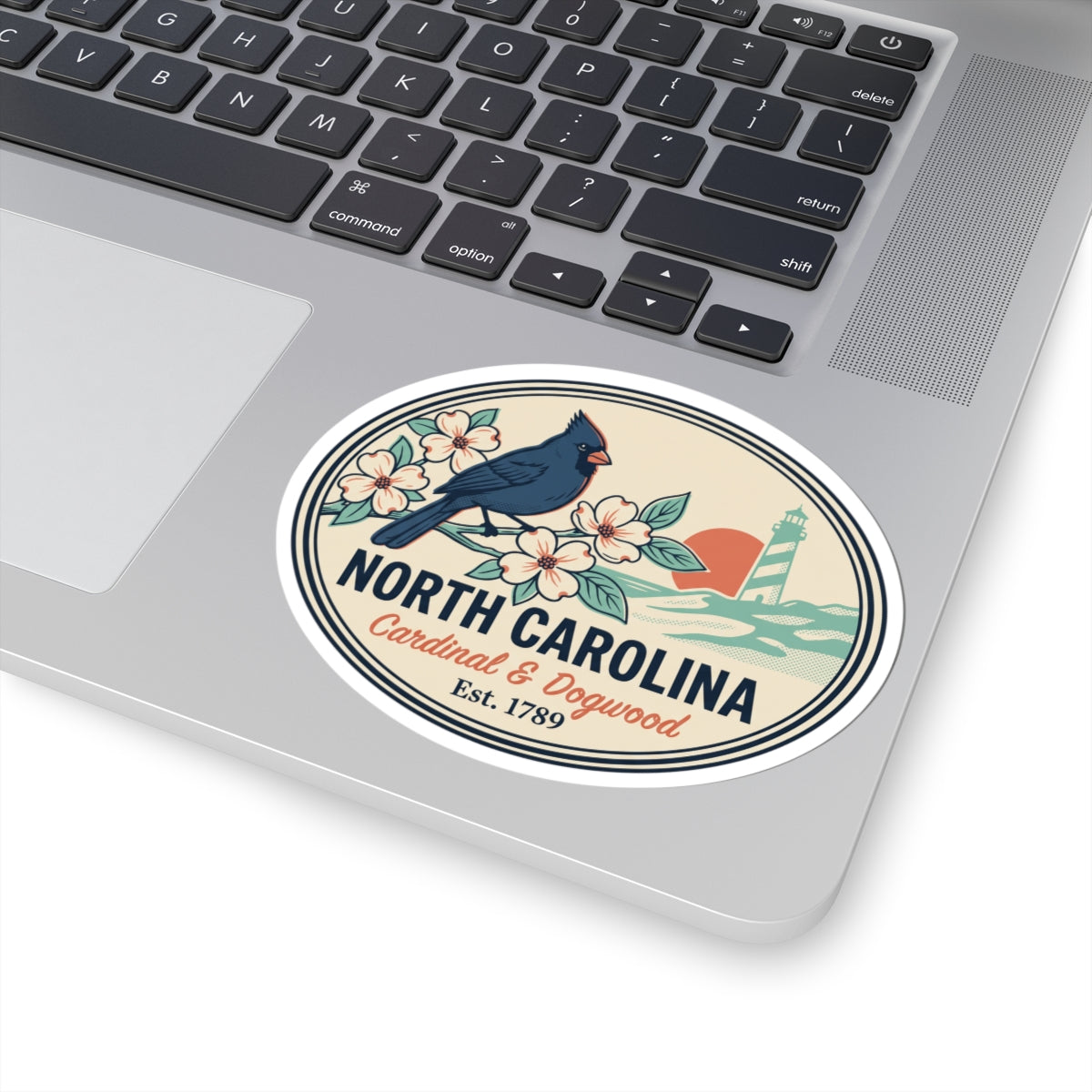 North Carolina state badge sticker on laptop keyboard, showing cardinal, flowers, lighthouse, text