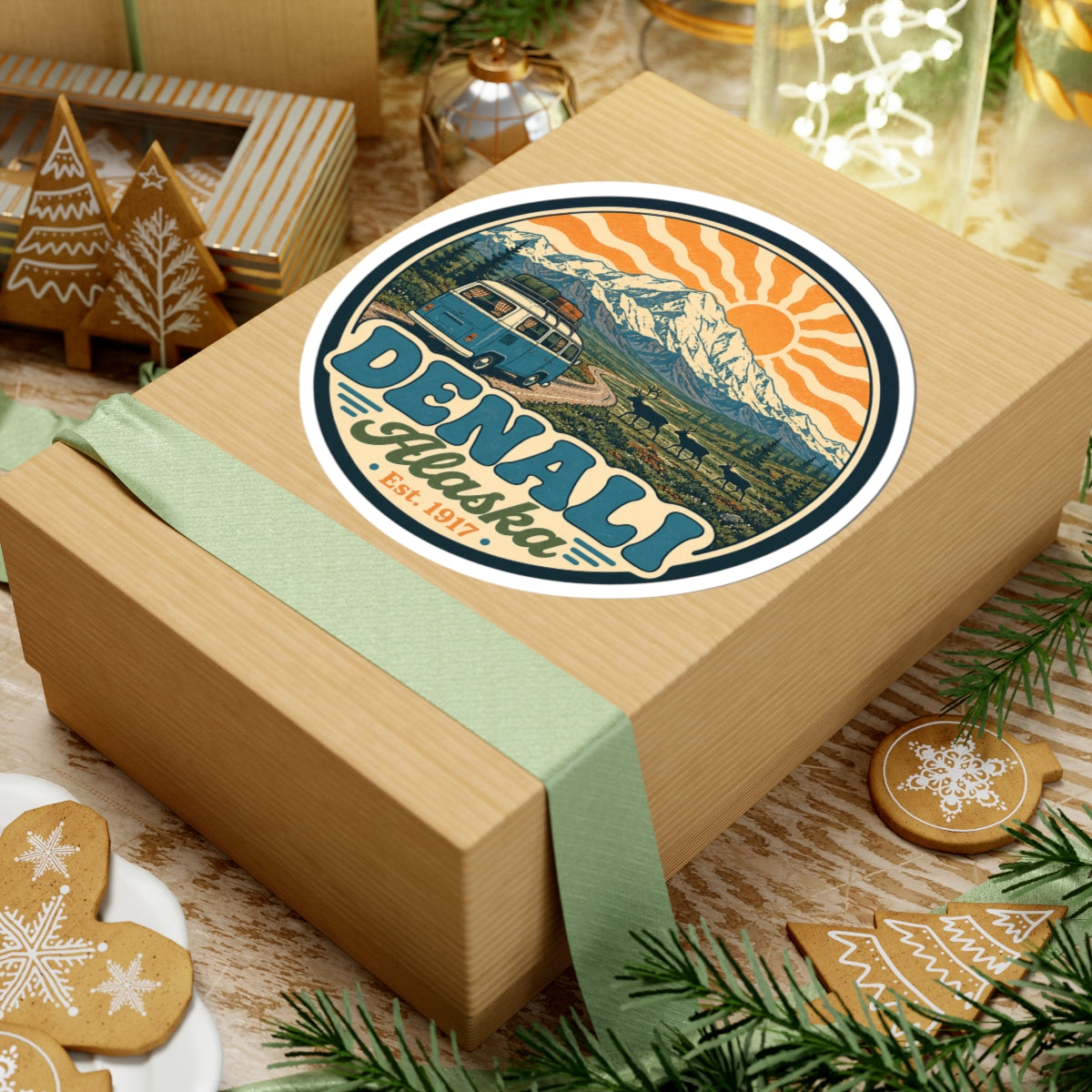 Round Denali Alaska sticker on a gift box, mountain scenery, sun rays, and teal camper van