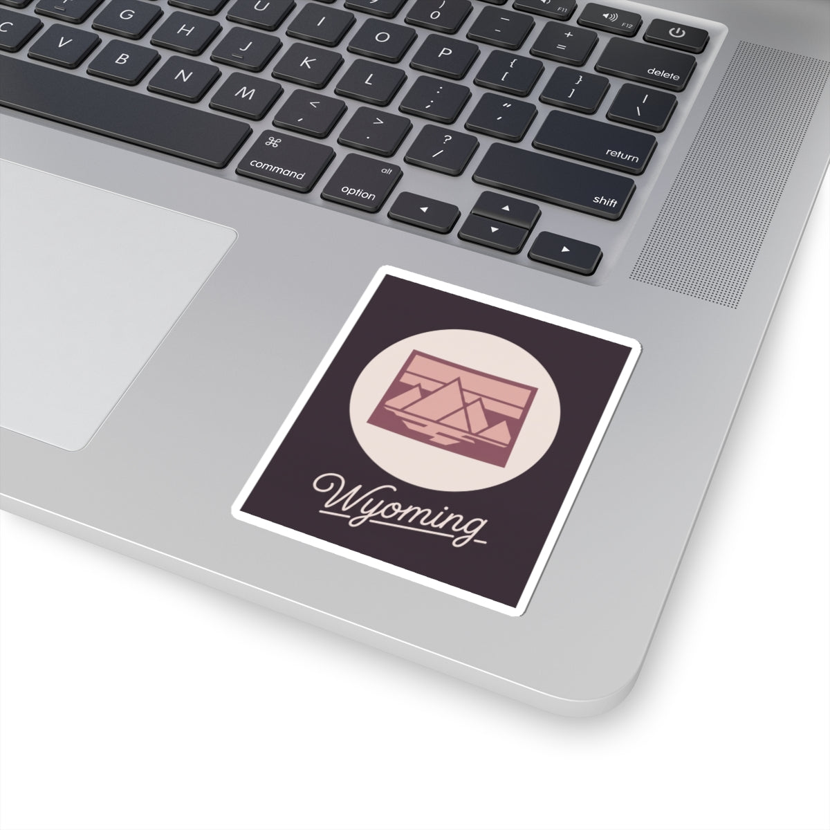 Wyoming sticker on laptop showing pink landscape graphic and cursive “Wyoming”