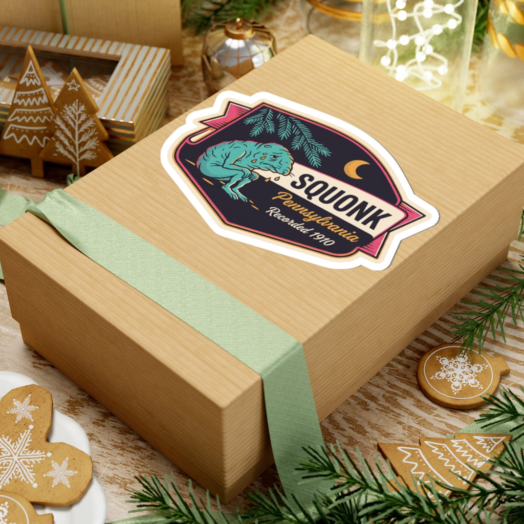 Kiss-cut Squonk Pennsylvania badge sticker on wrapped gift box, teal cryptid with pine