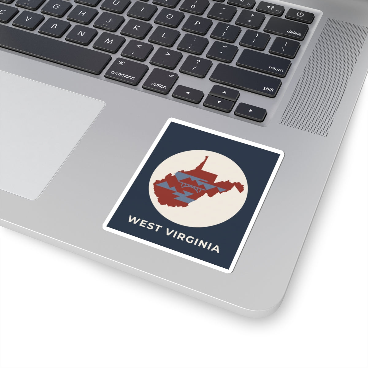 West Virginia map sticker on laptop keyboard, navy square with red state graphic and text