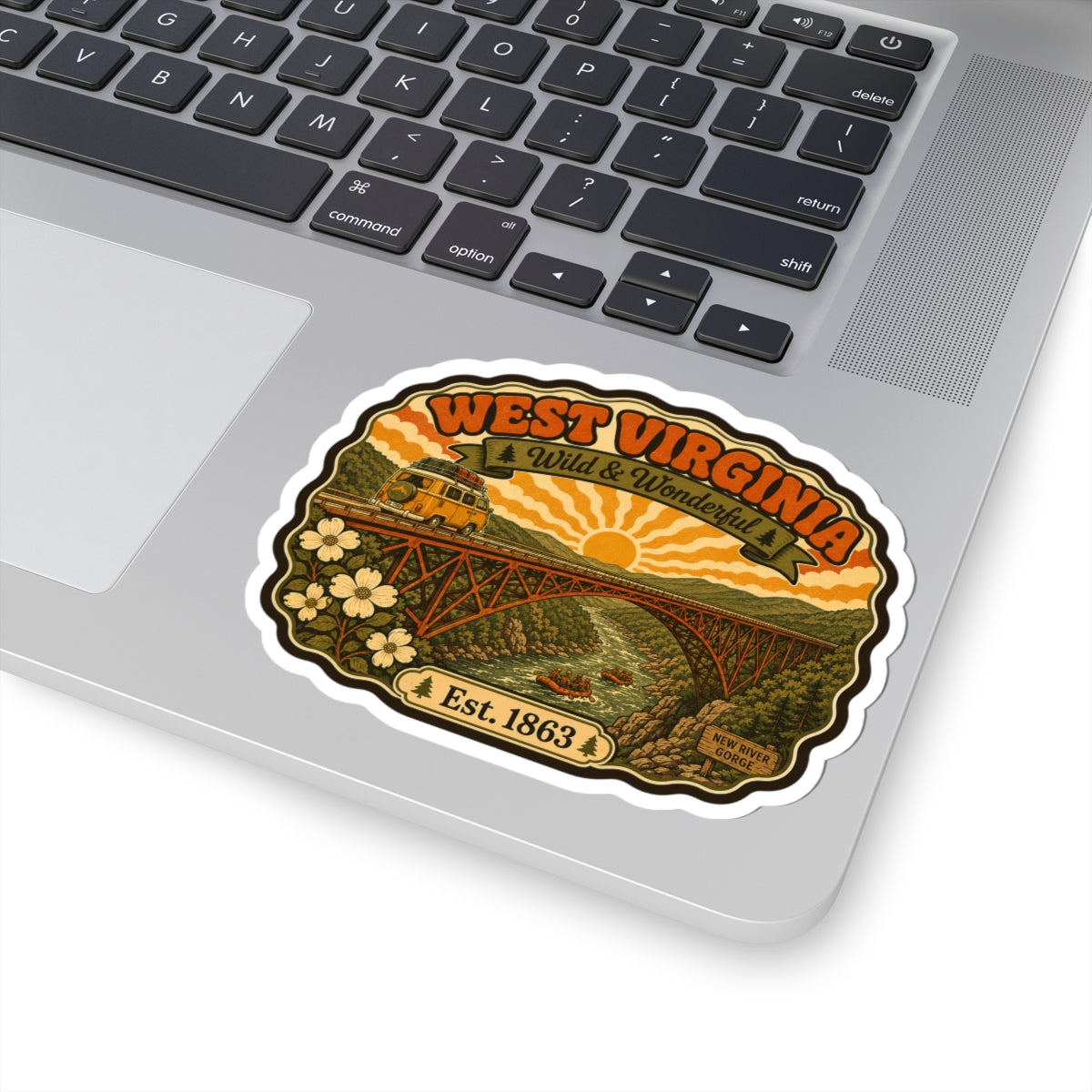 West Virginia kiss-cut sticker on a laptop, showing orange title, bridge, and Est. 1863.