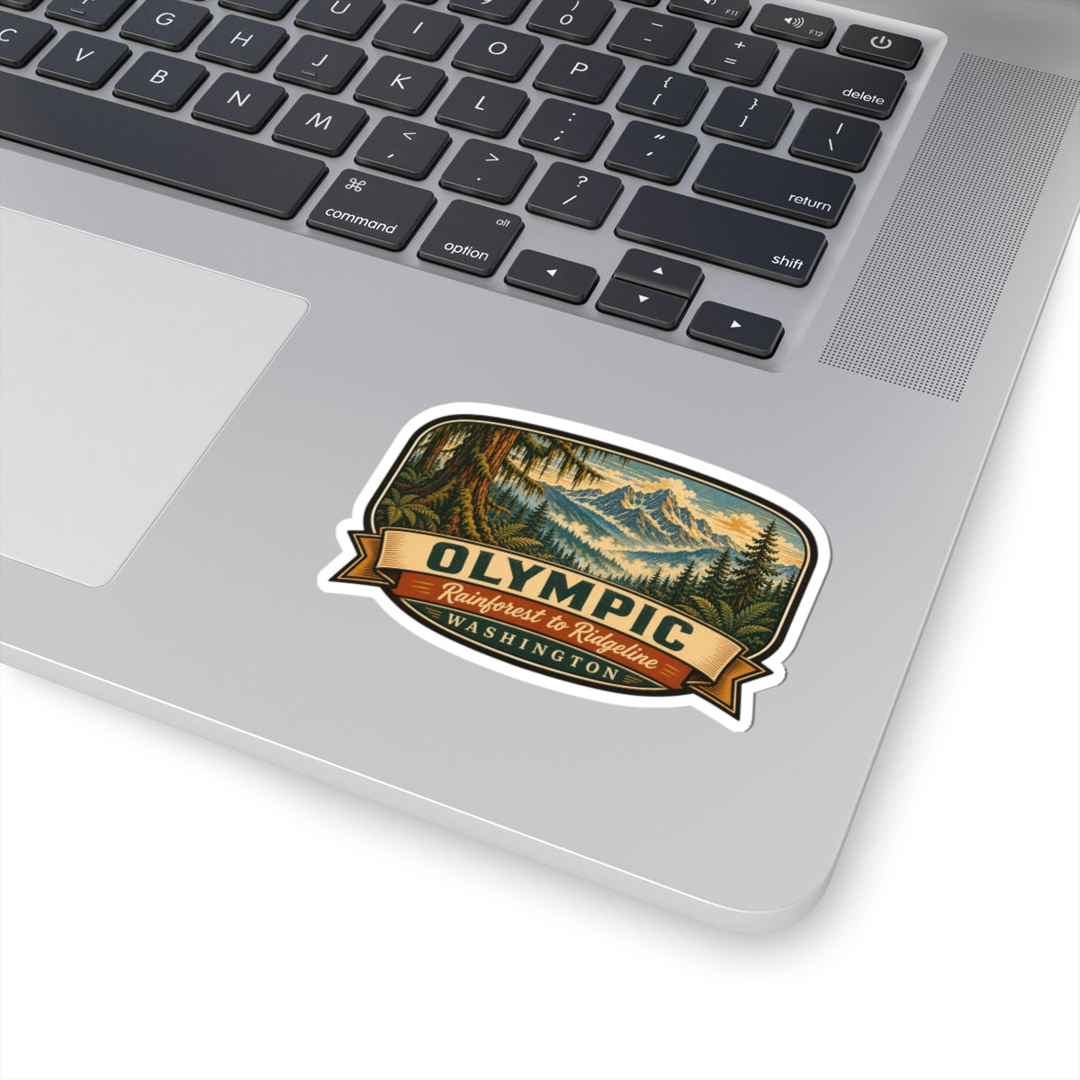 Olympic Washington travel sticker on laptop lid, showing mountain forest graphic and ribbon text